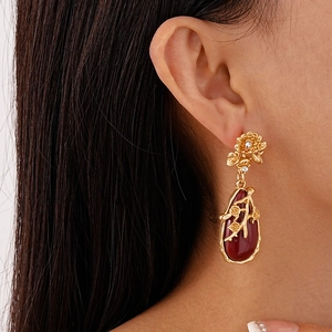 Vue détaillée de boucles d'oreilles fleur dorée avec goutte rouge sur un mannequin