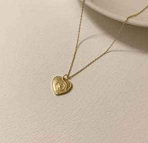 Macro shot of gold heart pendant necklace with engraved lettering on textured surface
