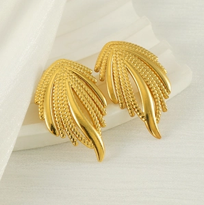 Vue rapprochée de boucles d'oreilles ailes dorées avec détails texturés sur tissu blanc