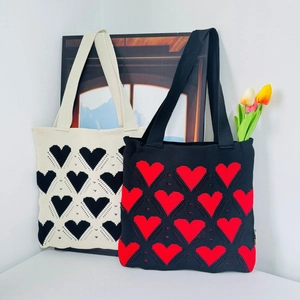 Detail of knitted tote bags featuring heart patterns in cream and black colors