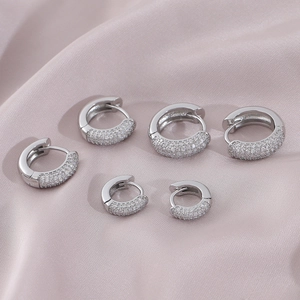 Three pairs of iced out silver hoop earrings in varying sizes on purple silk