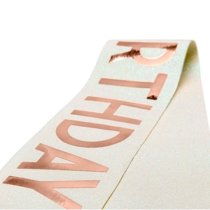 Close-up of birthday sash with rose gold foil lettering on ivory glitter fabric texture