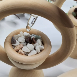 Close-up of glass dropper adding essential oil to stones inside the wooden ring diffuser