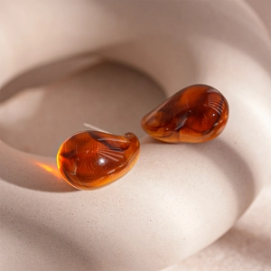 Détail de boucles d'oreilles en résine ambrée montrant la texture lisse et veinée