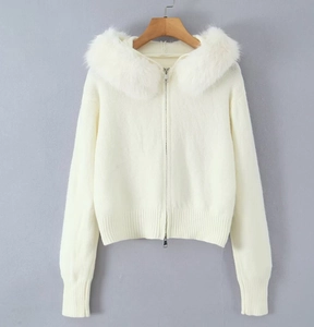 Detailed close-up of a white knit cardigan with a fluffy faux fur collar and dual metal zippers