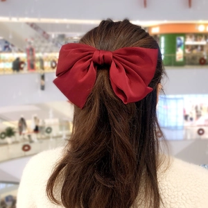 Detail of a large burgundy satin bow hair clip on a model showing back of head style