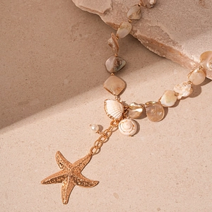 Macro detail of gold starfish and white seashell pendants on a beaded ocean necklace