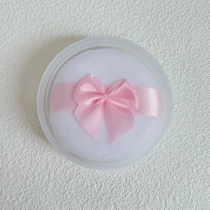 Close-up of white crystal velvet powder puff with pink bow in a clear round storage case
