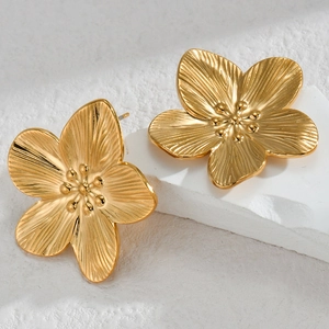 Macro detail of 18K gold flower stud earrings with radial texture on a white stone