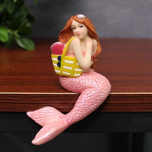 Creative resin mermaid girl figurine with pink scales sitting on a wooden desk edge decoration