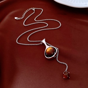 Détail du collier argenté avec pierres brunes sur tissu rouge foncé texturé