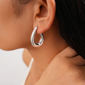 Detailed close-up of a large polished silver teardrop earring on a model's ear