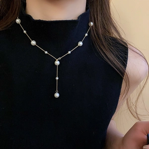Detail showing the elegant gold tassel pearl necklace worn on a black turtleneck sweater