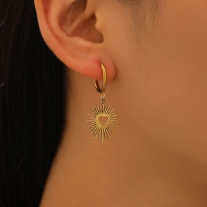 Détail de boucles d'oreilles dorées avec pendentif soleil et cœur évidé sur le modèle