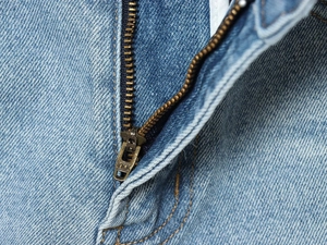 Dettaglio ravvicinato della cerniera metallica YKK su jeans in denim di cotone blu