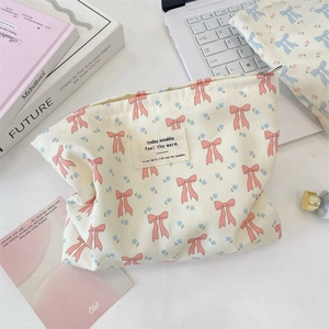 Flat lay of floral canvas makeup bags with pink bows on a minimalist desk setup