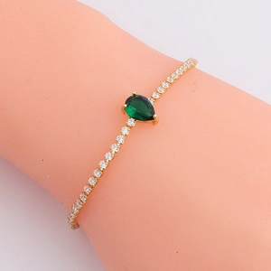 Detailed view of a gold-plated bracelet with a large green pear-cut zircon on the wrist