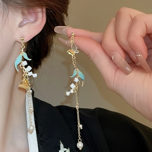 Detailed view of long tassel earrings with golden butterfly, blue leaf and pearl charms