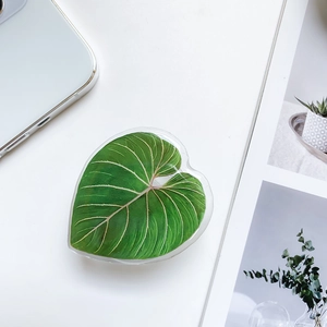 Macro shot of heart-shaped phone grip with green leaf pattern on white minimalist desk