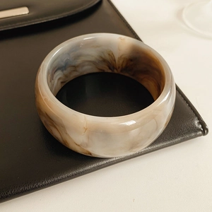 Detailed macro of wide resin bangle with marble texture on black leather bag