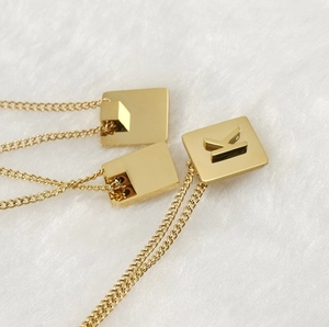 Detailed view of 18K gold plated square pendants with letter K on white faux fur background