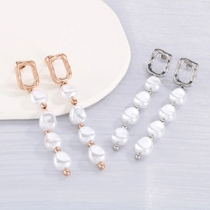 Détail de boucles d'oreilles géométriques en or rose et argent avec perles blanches