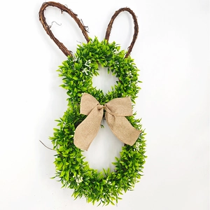 Detail of Easter bunny wreath showing green leaves, rattan ears, and a burlap bow