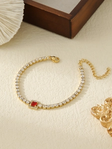 Detailed close-up of gold tennis chain bracelet with white zircons and red square gemstone