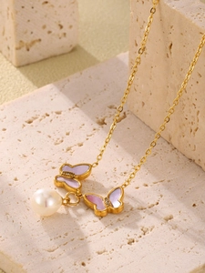 Gros plan sur le collier papillon doré avec des ailes en nacre violette et une perle