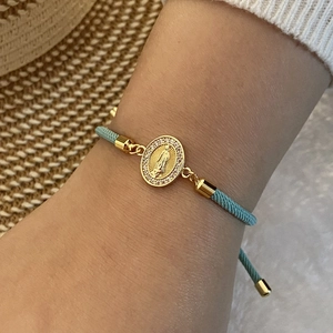 Detail of blue braided bracelet featuring a 18K gold Virgin Mary oval charm with zircons