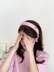 Dettaglio del cerchietto imbottito rosa con logo dorato su tessuto tweed strutturato