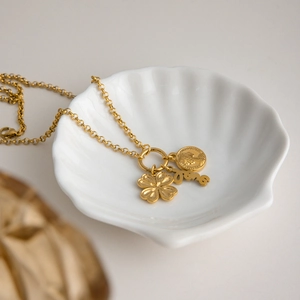 Detail view of 18K gold plated clover coin and love pendants in a shell plate