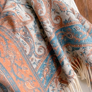 Close-up of knit paisley scarf with orange and blue patterns and fringed tassel details