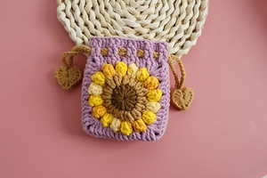 Macro detail of purple crocheted mini drawstring pouch with 3D sunflower and heart decor