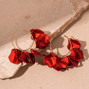 Detail of red petal hoop earrings with gold metal rings on a textured beige stone background
