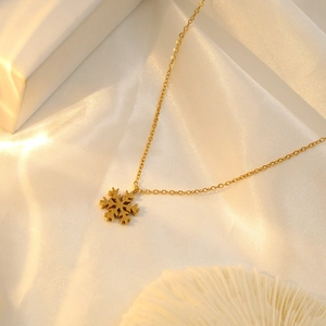 Detailed view of an 18k gold snowflake pendant necklace on soft fabric background
