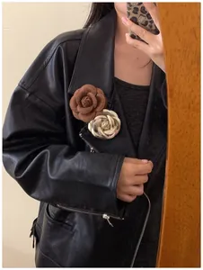 Close-up of velvet brown camellia and metallic gold flower brooches on a black leather jacket