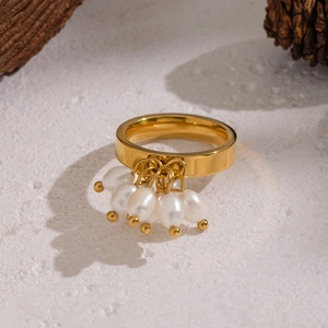 Detail eines vergoldeten Edelstahlrings mit weißen Perlenanhängern und natürlichen Zapfen