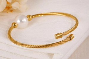 Détail d'un bracelet jonc doré en câble d'acier avec une grande perle blanche