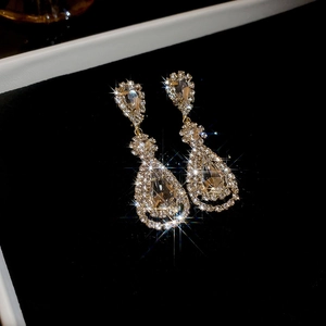 Macro shot of gold teardrop tassel earrings with white crystals on black velvet