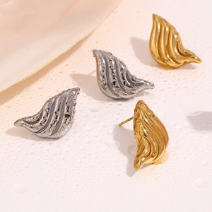 Detailed view of textured metal wing earrings in gold and silver on a water droplet surface