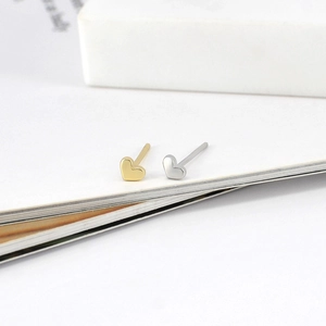 Detailed macro view of minimalist heart stud earrings in polished gold and silver finishes