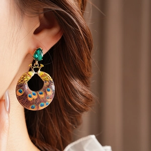 Close-up of vintage peacock feather enamel earring with green teardrop gem on model