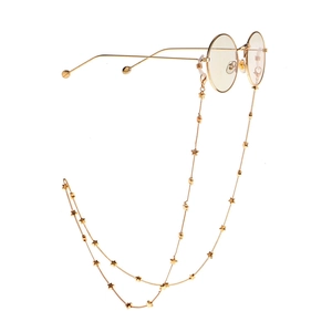Macro detail showing gold star charms on a delicate metal eyewear chain with round frames