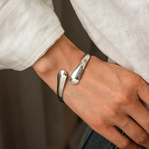 Polished silver open cuff bracelet with teardrop ends styled on a wrist