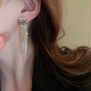 Elegante lange Fransenohrringe mit weißen Perlen und glitzernden Straßsteinen am Model