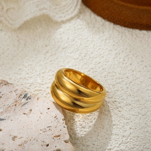 Close-up of a chunky 18K gold double-layered ring on a textured beige stone background