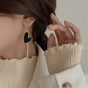 Close-up of asymmetrical golden earrings with black hearts and fringe on model