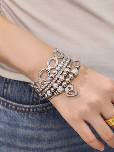 Gros plan de bracelets en acier inoxydable argenté superposés avec breloque cœur au poignet