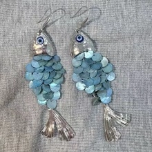 Dettaglio di orecchini a forma di pesce creativi con squame iridescenti blu e perline